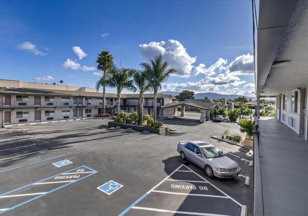 An exterior view of a motel parking lot with a silver car parked near an accessible parking space under a blue sky.