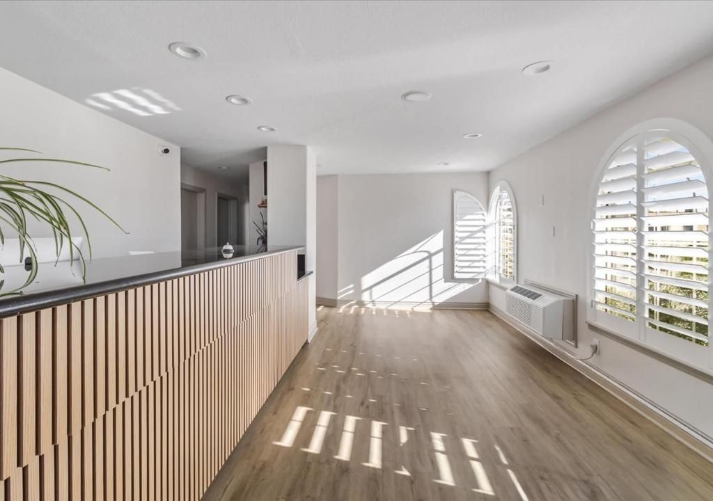 A bright office interior with a light wood-slatted front desk, wood-look flooring, and arched windows with white shutters.