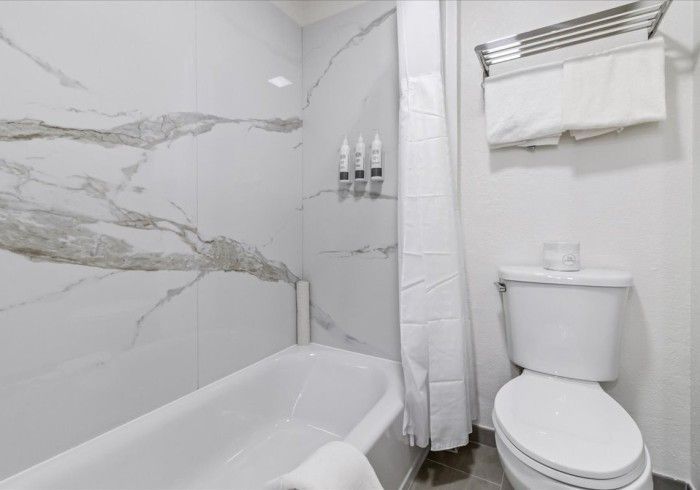 A bathroom featuring a white bathtub with marble-patterned tile walls, a shower curtain, a toilet, and towel rack.