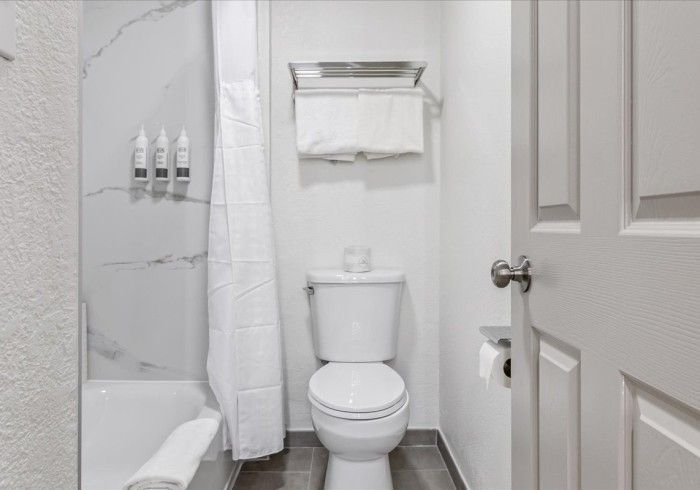 A modern bathroom featuring a white toilet, a marble-patterned shower area with wall-mounted bottles, and hanging towels.