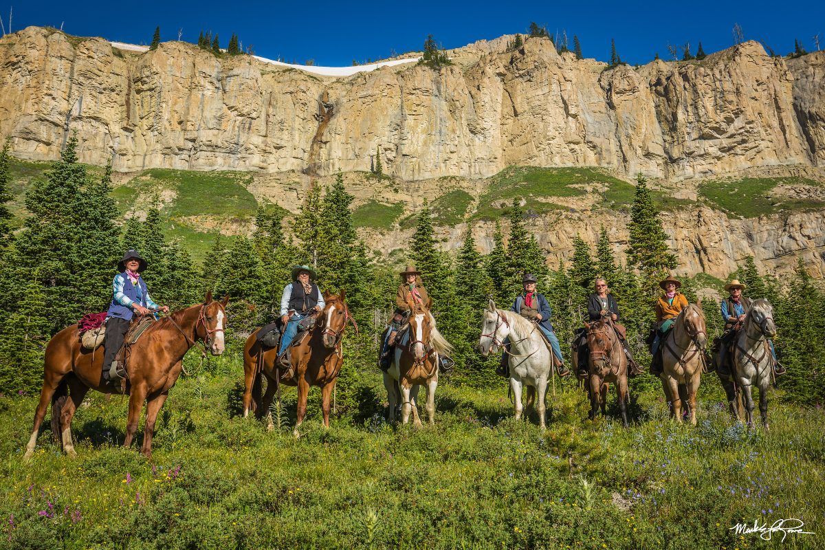 A group of people are riding horses in a field in front of a mountain.