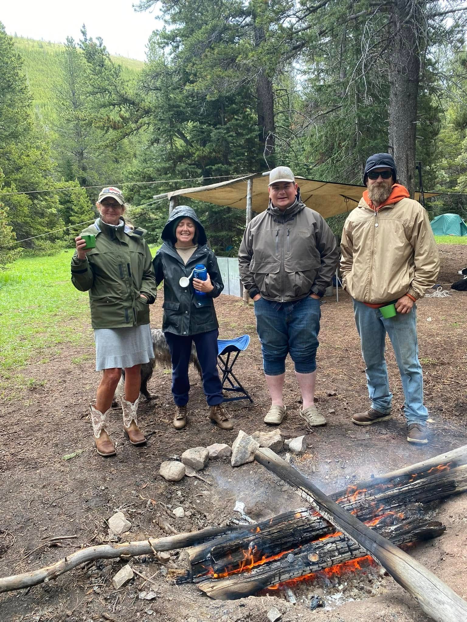 A group of people are standing around a campfire in the woods.