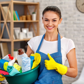 Person cleaning a wooden table with yellow gloves beside a potted plant.