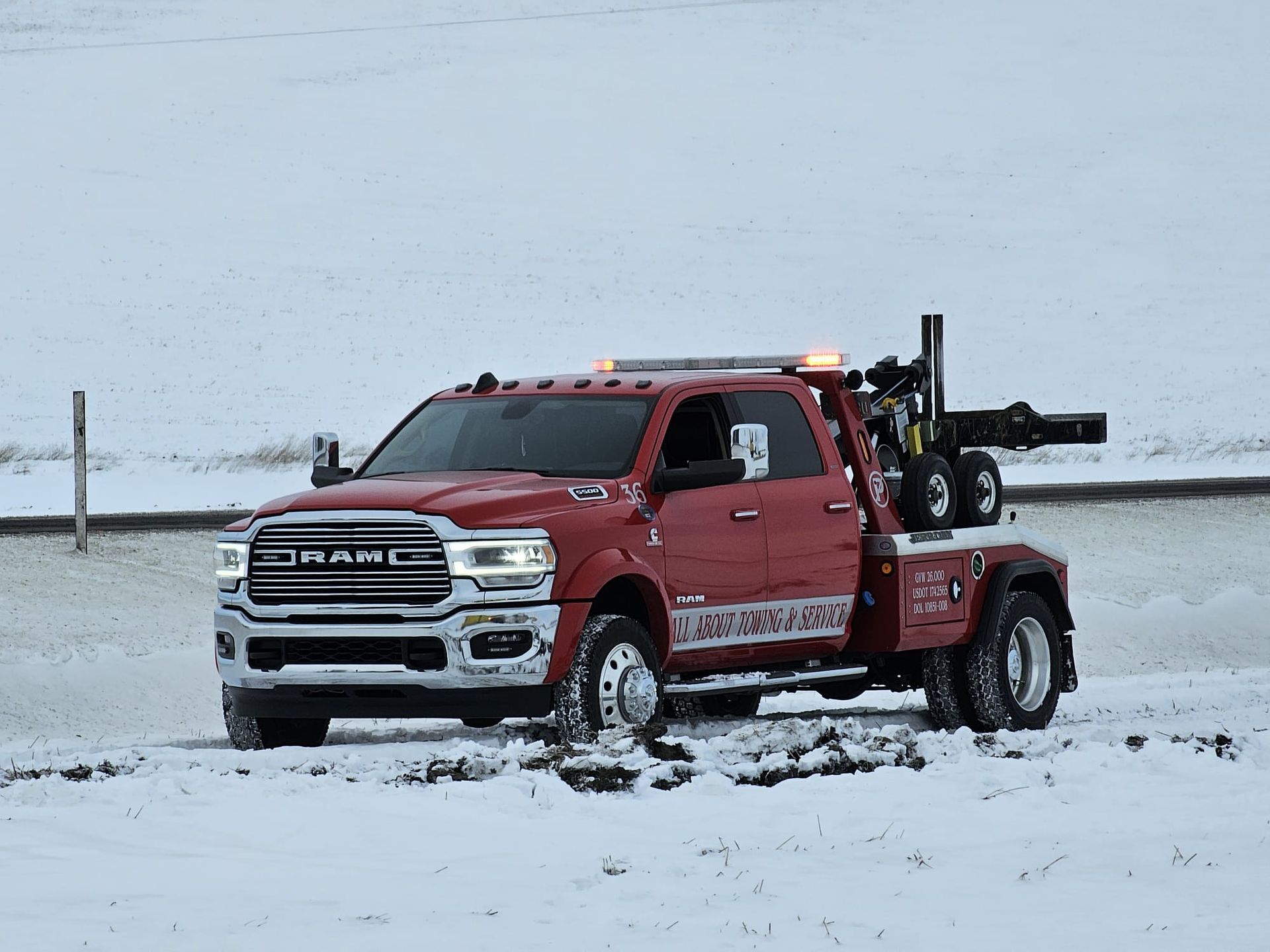 A red tow truck is parked in the snow on the side of the road.