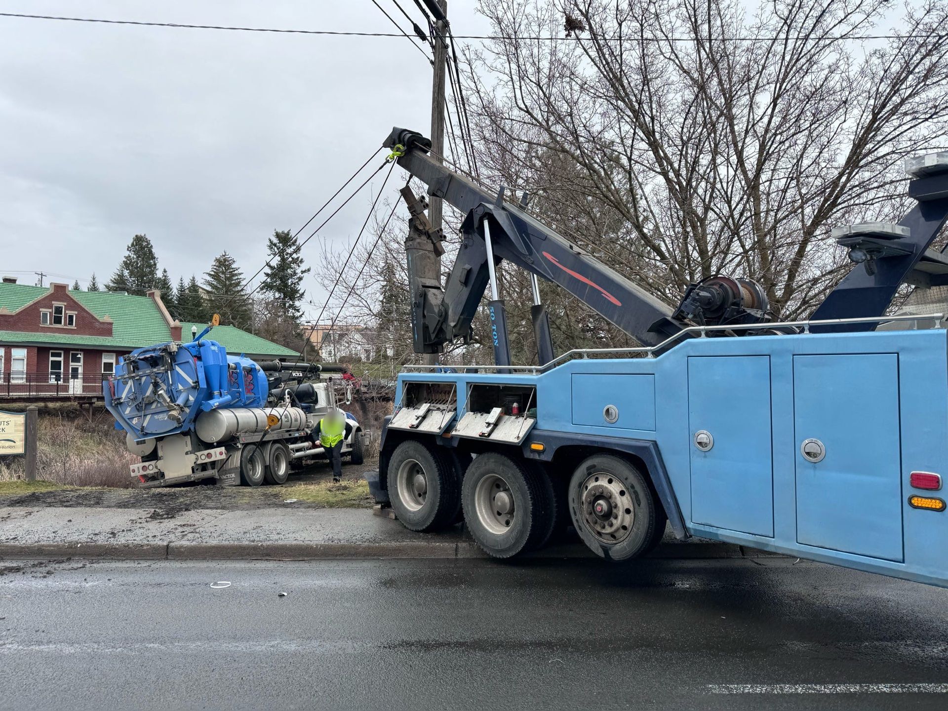 A blue tow truck is towing a truck on the side of the road.