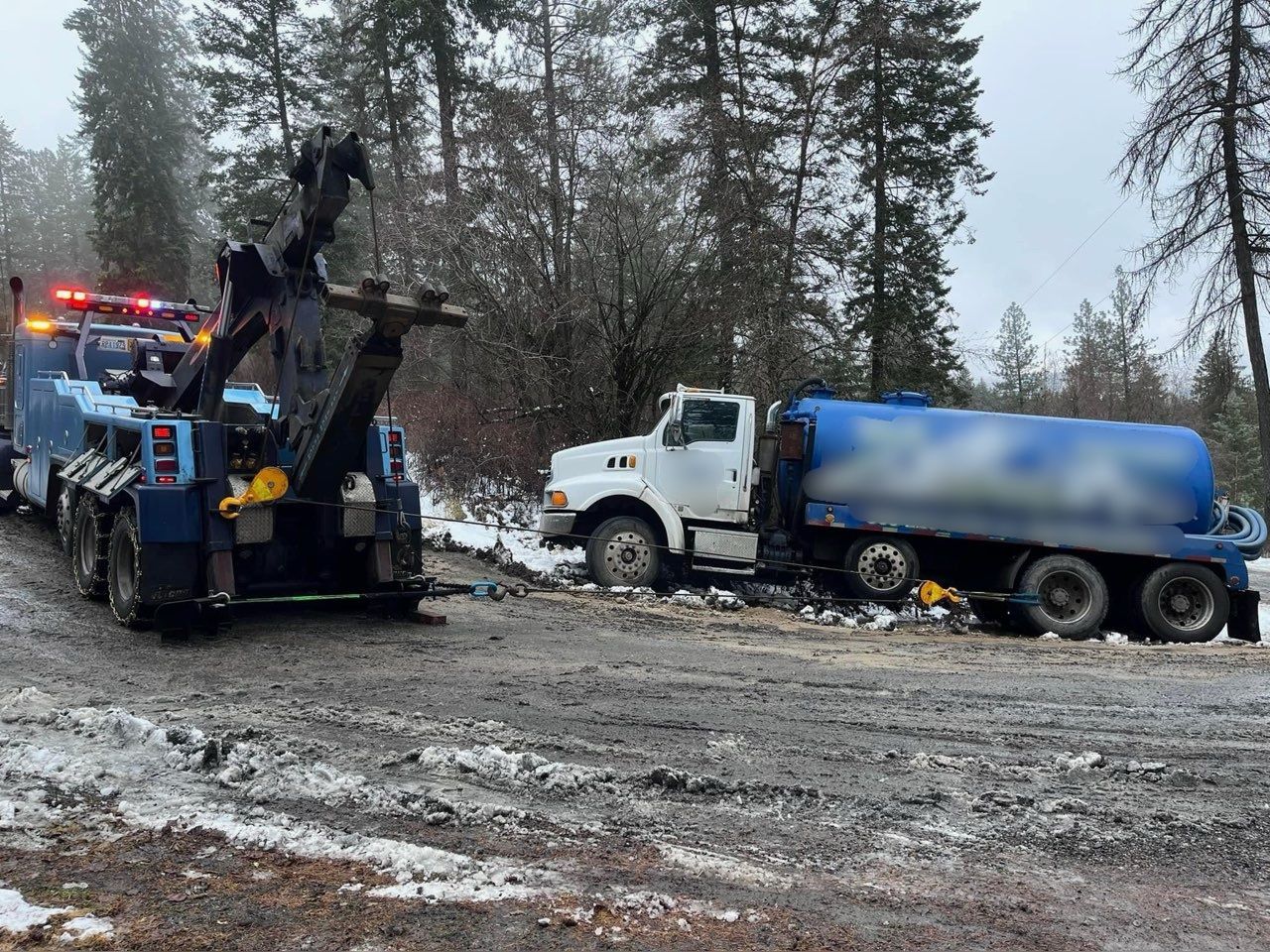 A tow truck is towing a tanker truck on a snowy road.