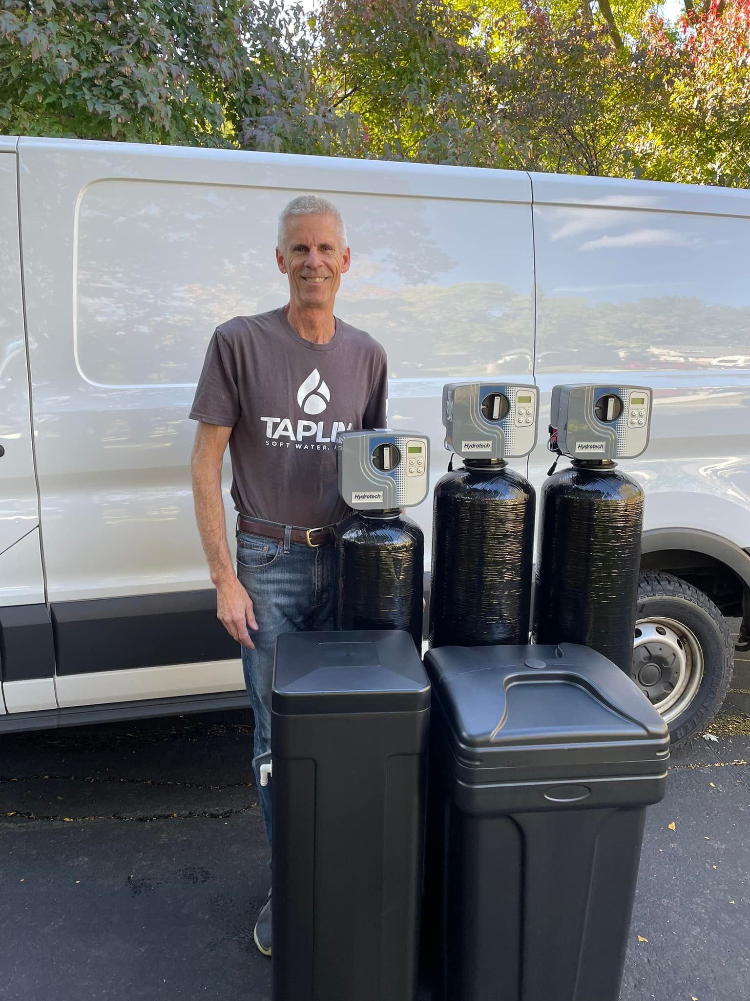 A man is standing in front of a van holding a water softener.