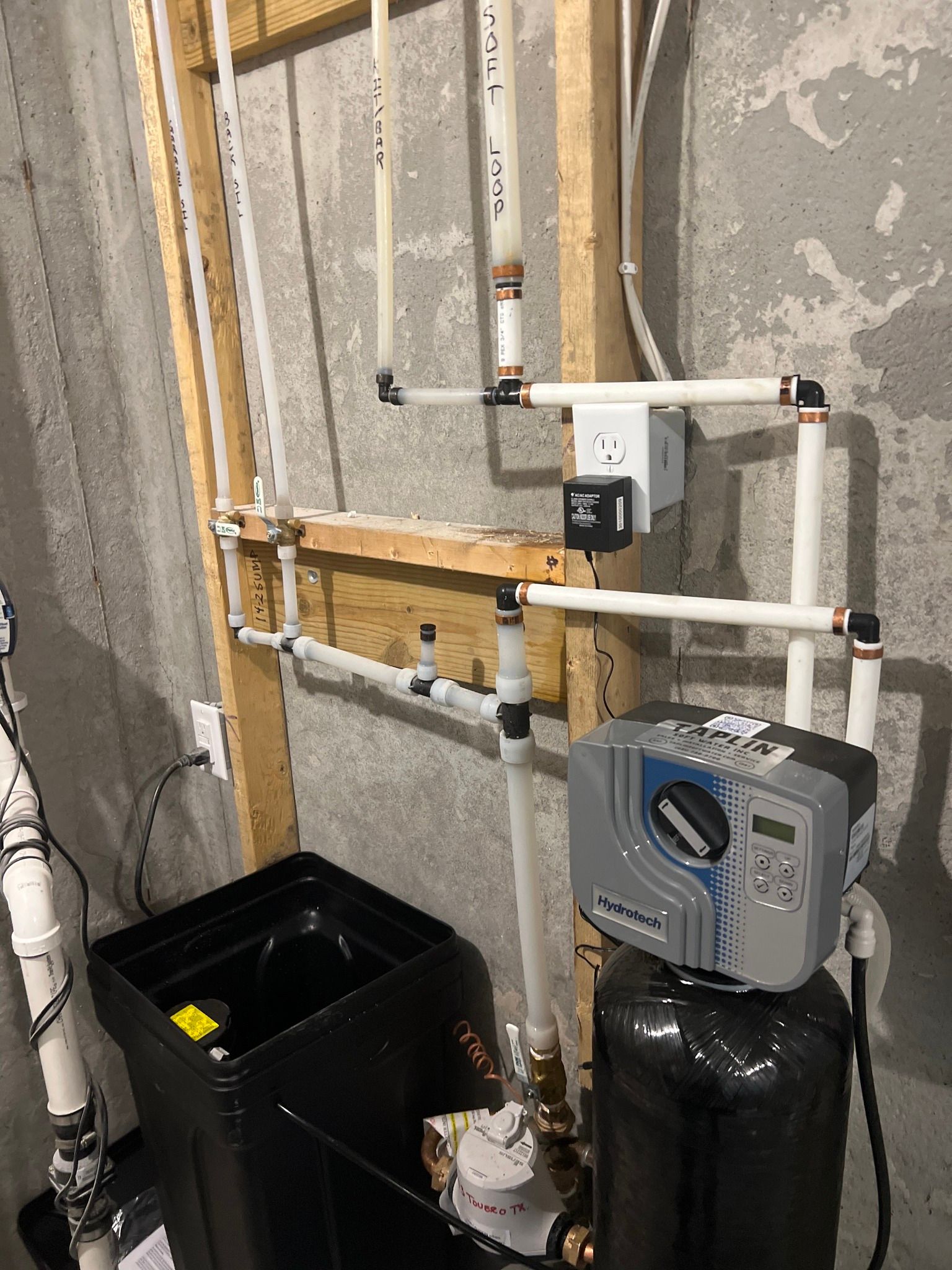 A water softener is sitting on top of a black tank in a basement.