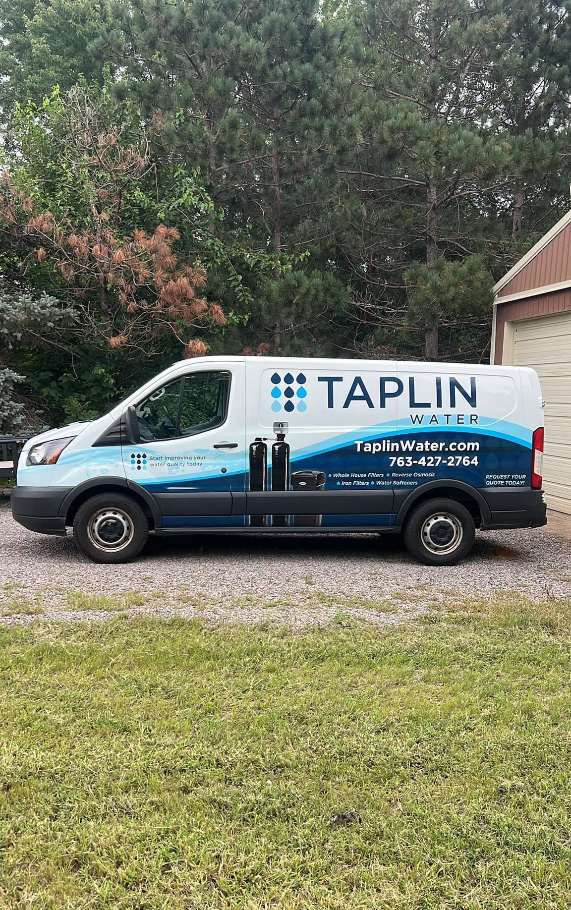 A taplin van is parked in a grassy area in front of a garage.