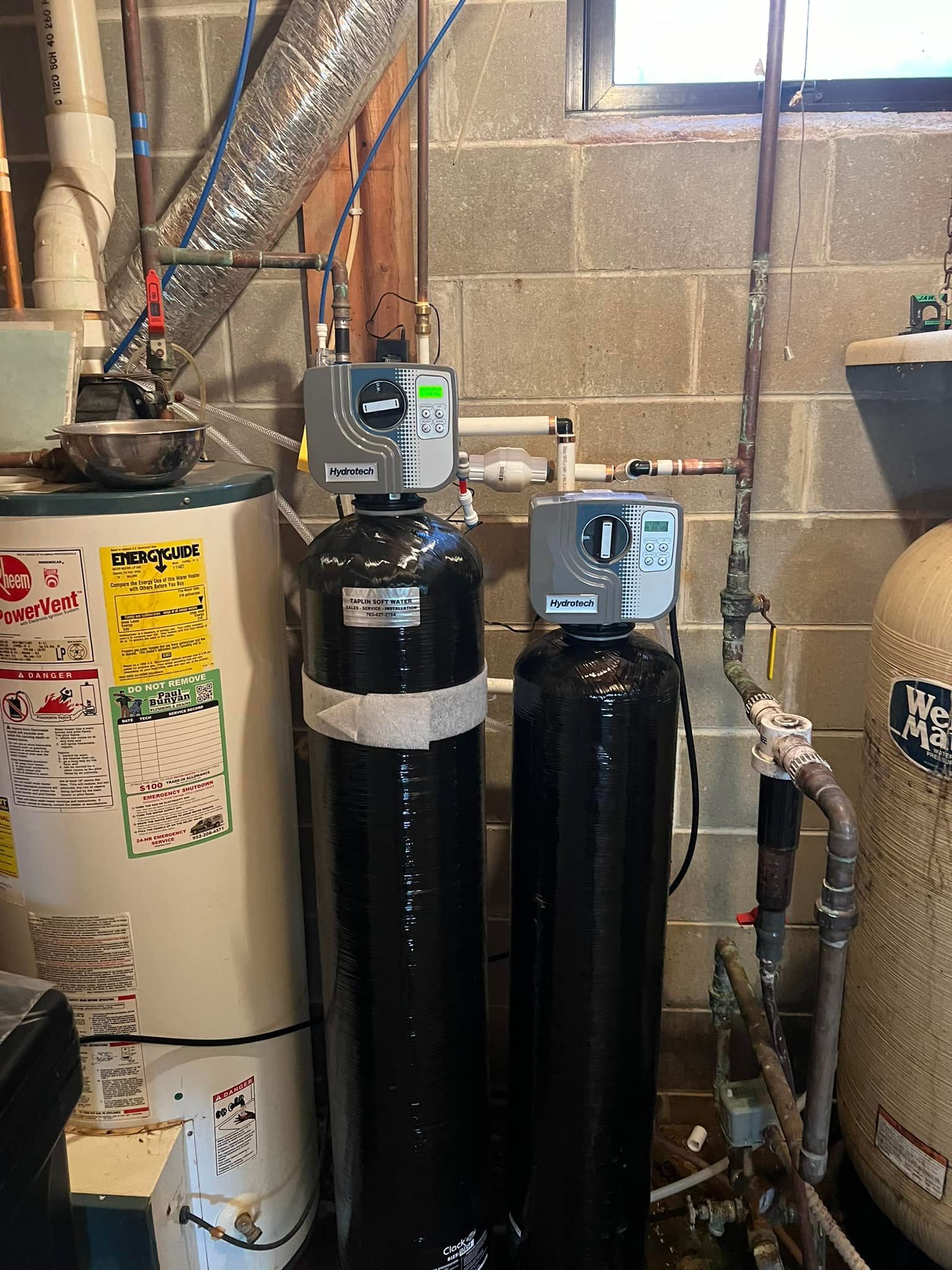 Two water heaters are sitting next to each other in a basement.
