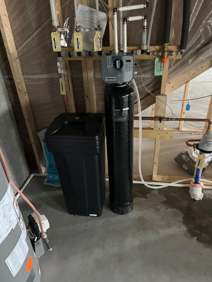 A water softener is sitting next to a trash can in a basement.