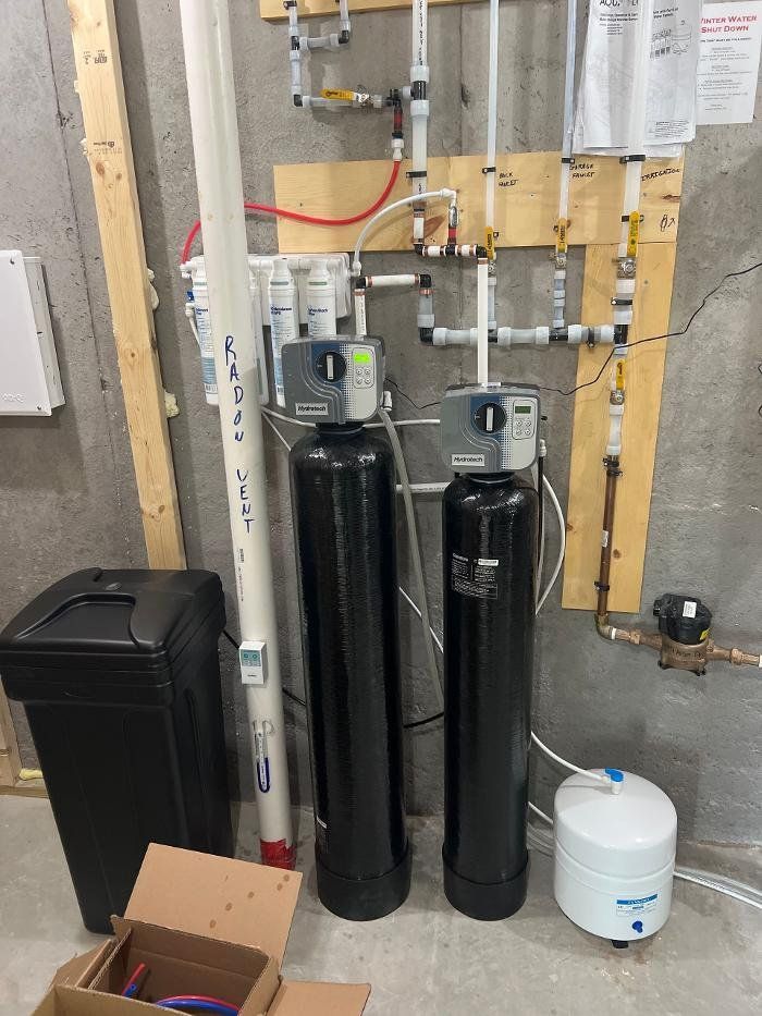 Two black water filters are sitting next to each other in a basement.