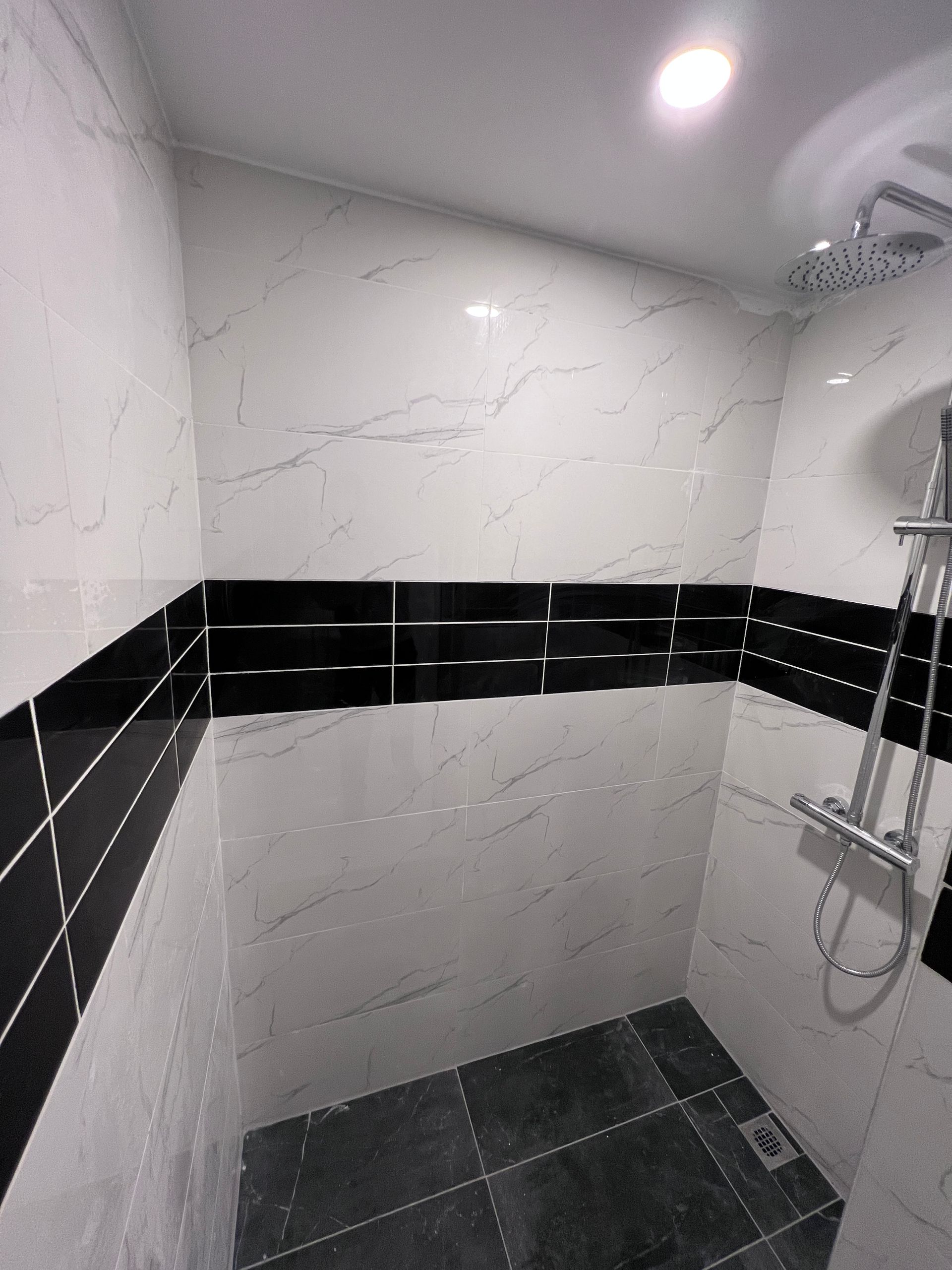 Une salle de bain avec carrelage noir et blanc et pommeau de douche.