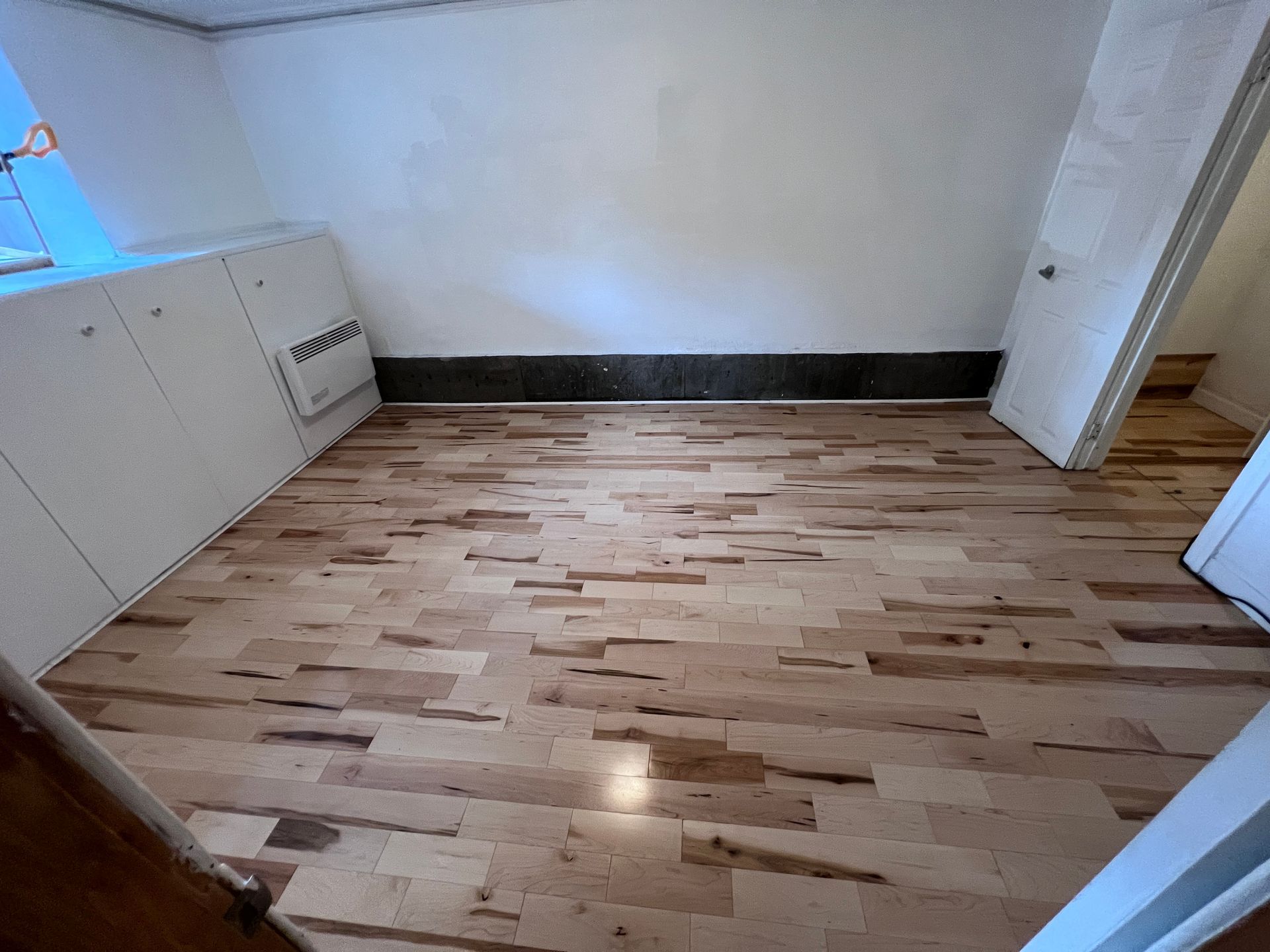 Une pièce avec un plancher en bois et des murs blancs.