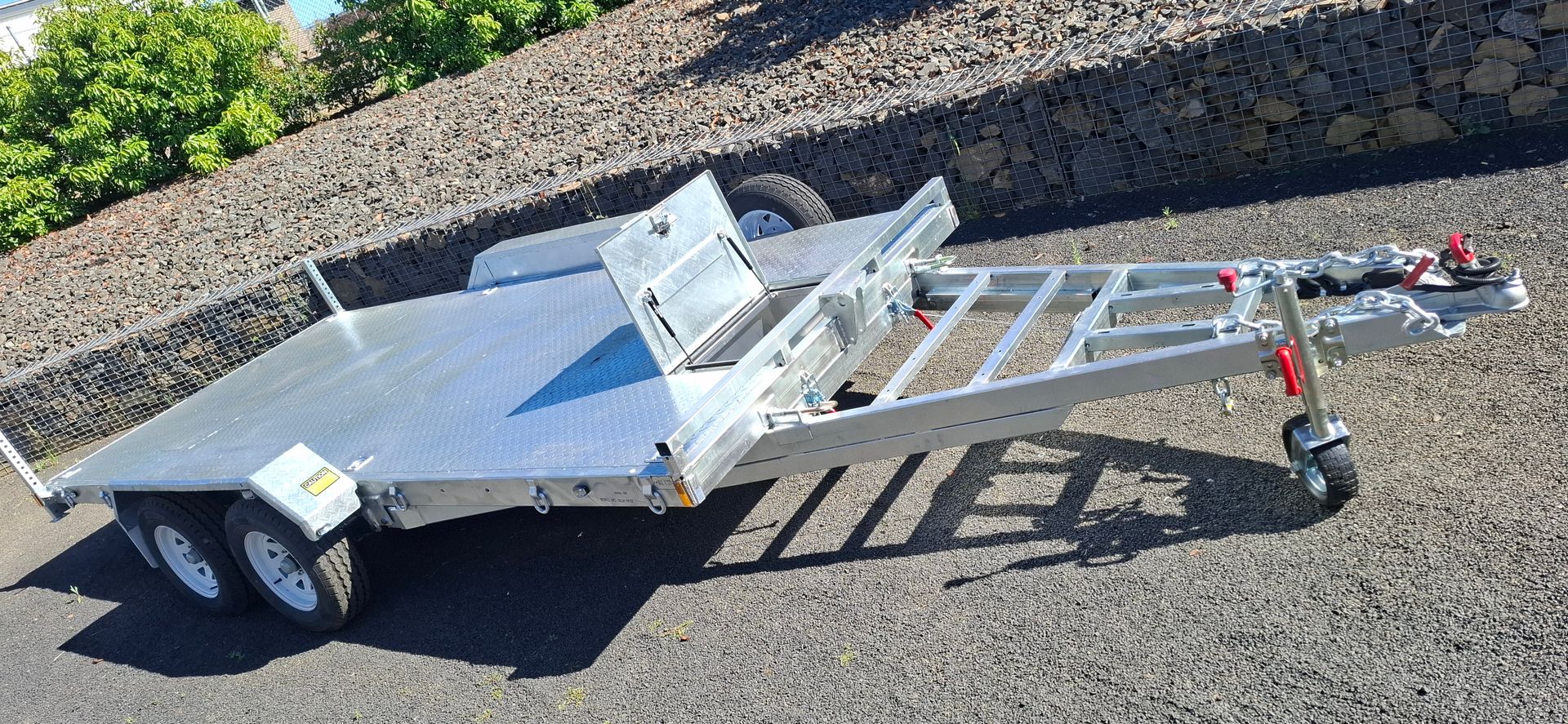 A silver, aluminum car trailer on a gravel surface next to a green hedge — Towform Trailers in Brocklehurst, NSW