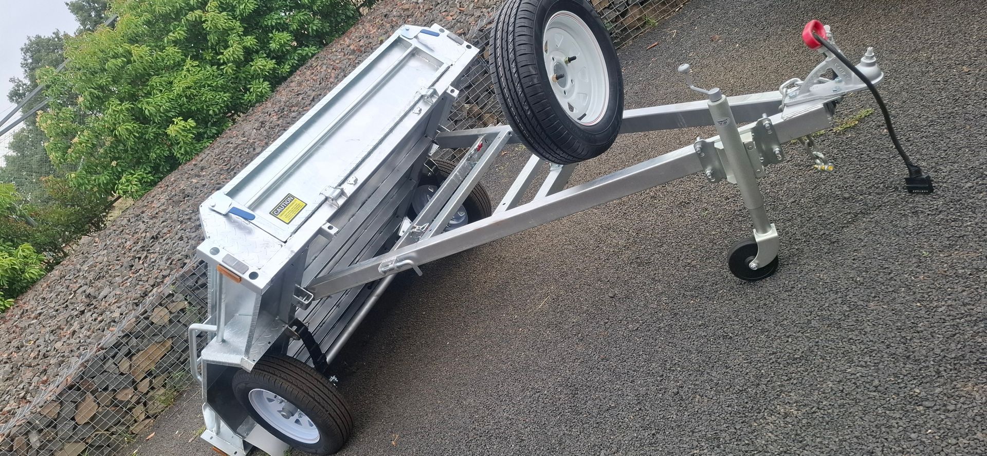 A silver utility trailer with two tires on a gravel surface — Towform Trailers in Brocklehurst, NSW