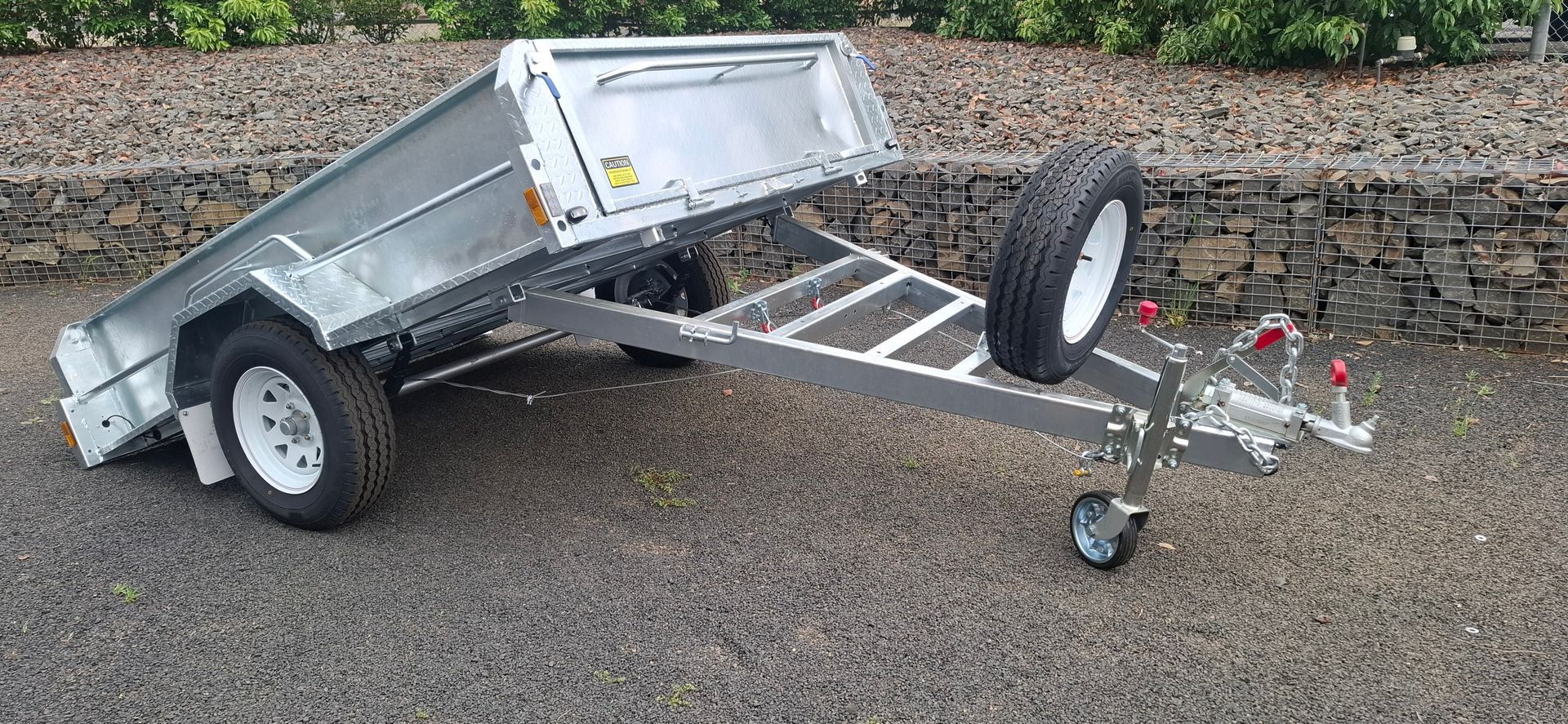 Silver utility trailer with two wheels and a spare tire on gravel — Towform Trailers in Brocklehurst, NSW