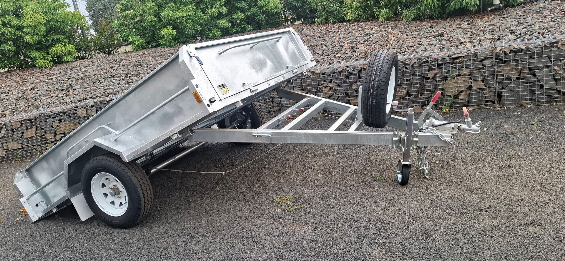 A silver utility trailer with the bed tilted upward with a spare tire attached — Towform Trailers in Brocklehurst, NSW