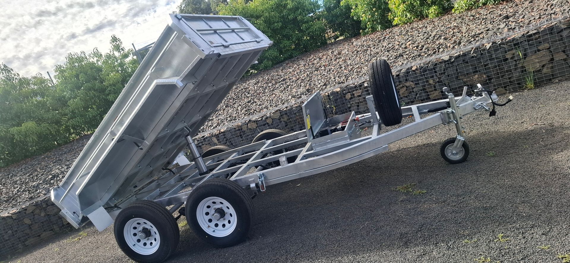A silver dump trailer tilted upward on a gravel driveway — Towform Trailers in Brocklehurst, NSW
