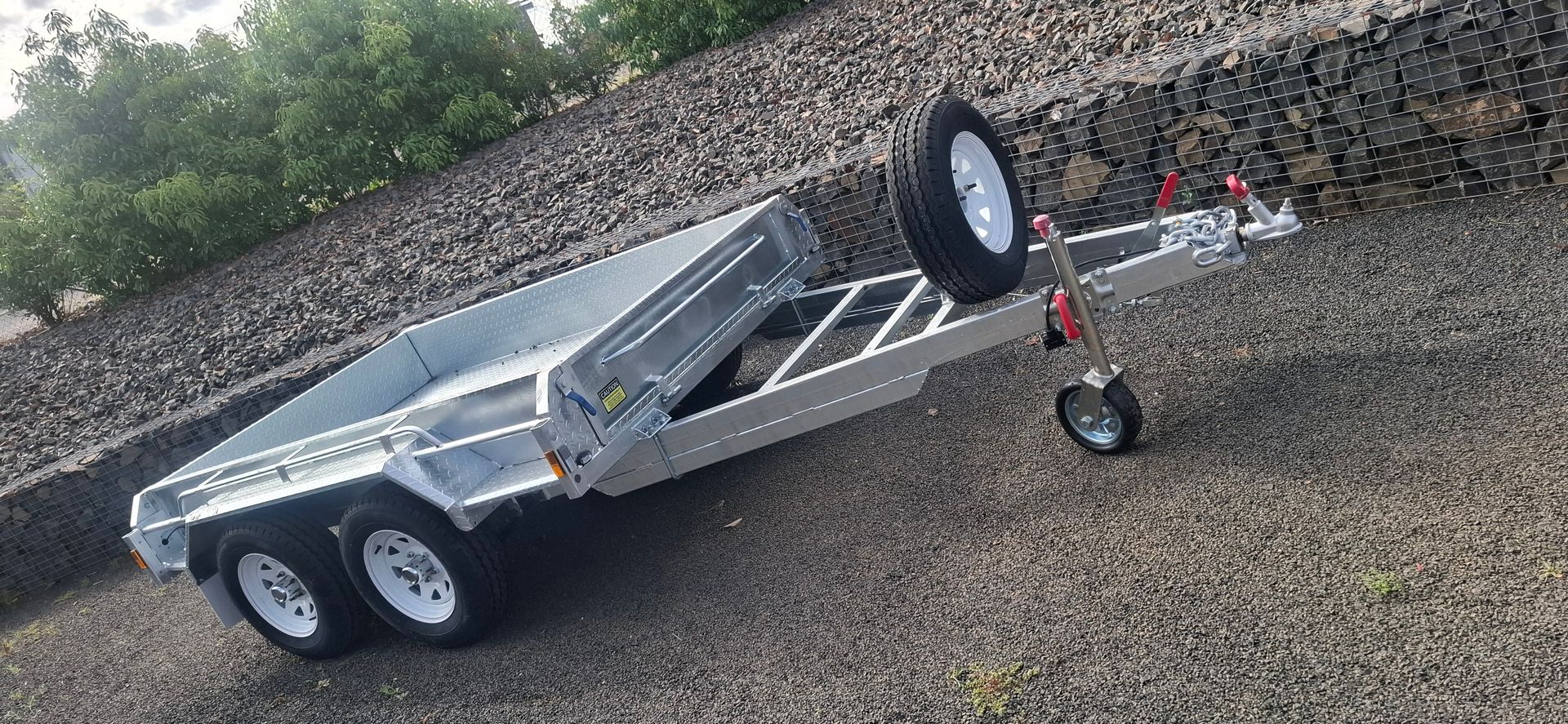 A silver trailer with three wheels is parked on gravel. A spare tire is mounted — Towform Trailers in Brocklehurst, NSW