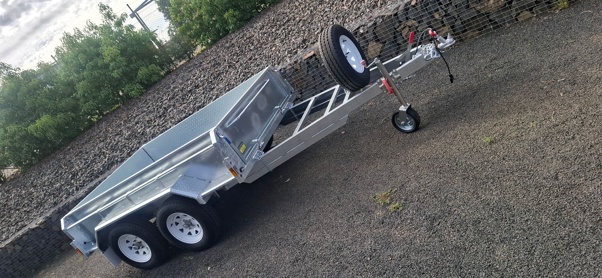 A gray utility trailer with three white wheels parked on a gravel surface — Towform Trailers in Brocklehurst, NSW