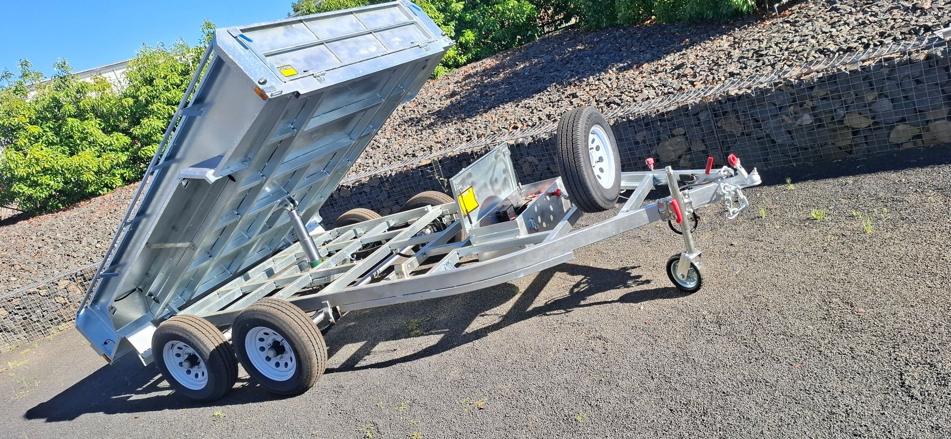 A silver dump trailer angled up on gravel with green foliage in the background — Towform Trailers in Brocklehurst, NSW