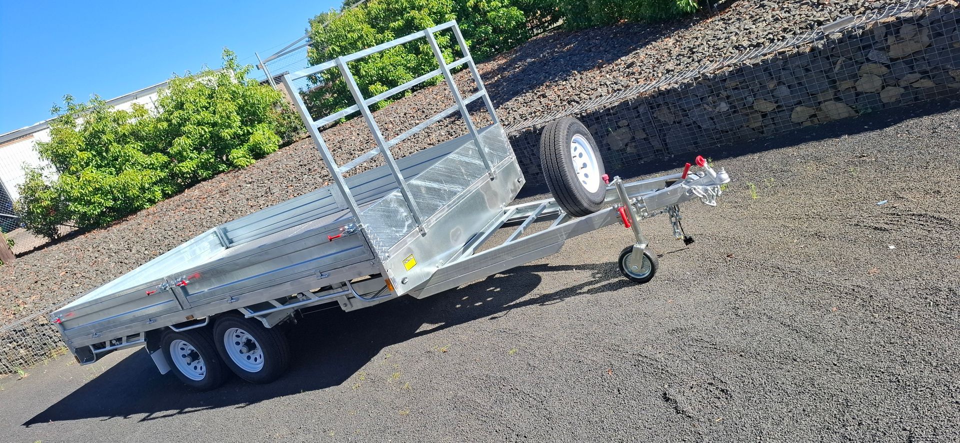 A Silver Flatbed Trailer With a Spare Tire on a Gravel Surface — Towform Trailers in Parkes, NSW