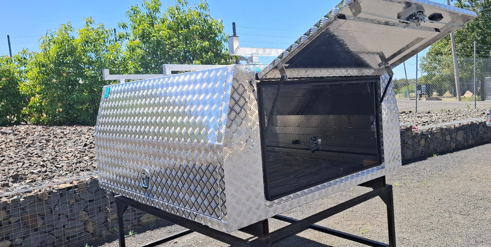 Diamond-plated aluminum tool box with open lid on a black metal stand — Towform Trailers in Brocklehurst, NSW