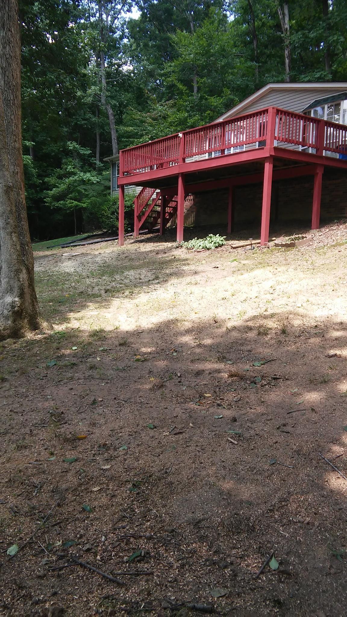 Deck with red railing and posts, built over a yard of brown mulch, backed by trees.