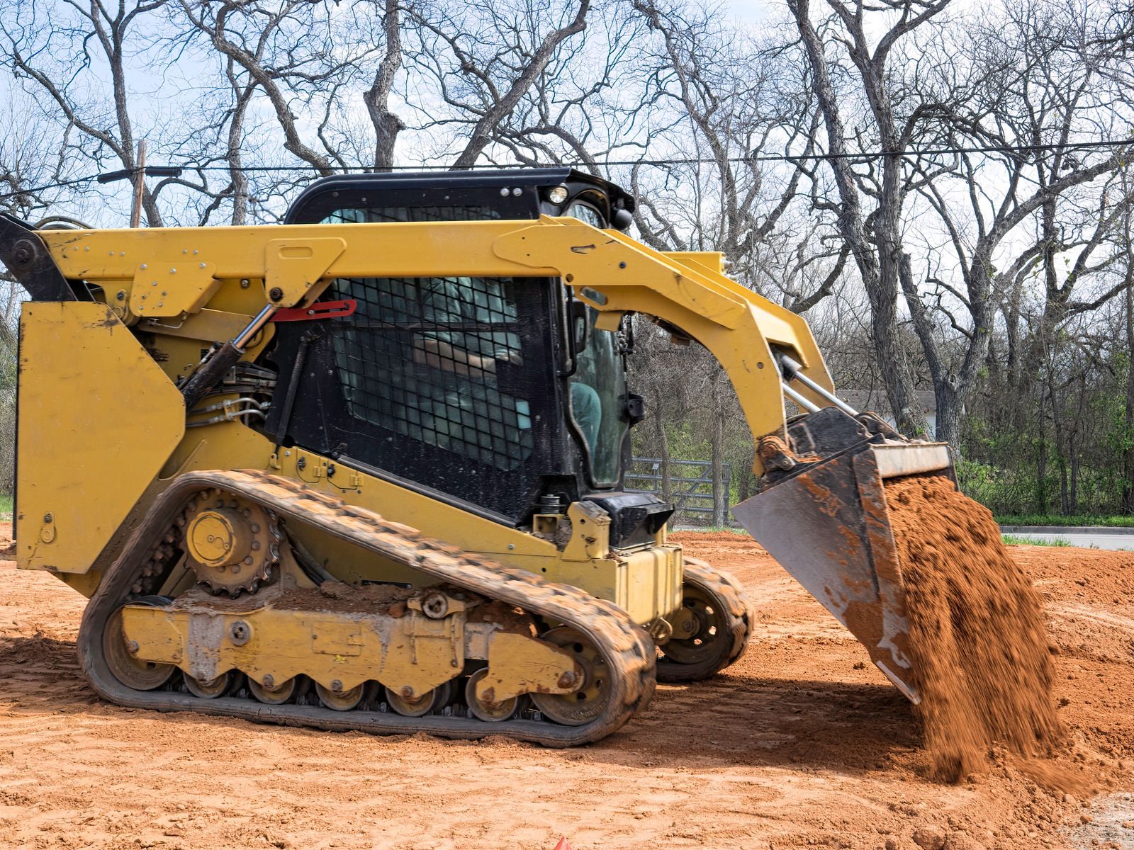 Yellow skid steer dumping dirt on a construction site.