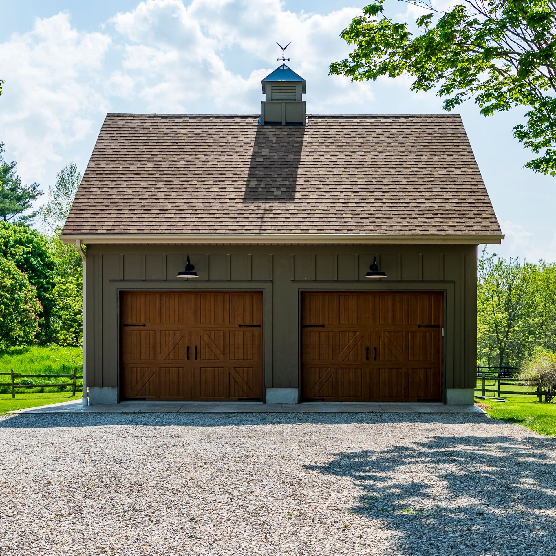 A garage with two wooden garage doors and a gravel driveway