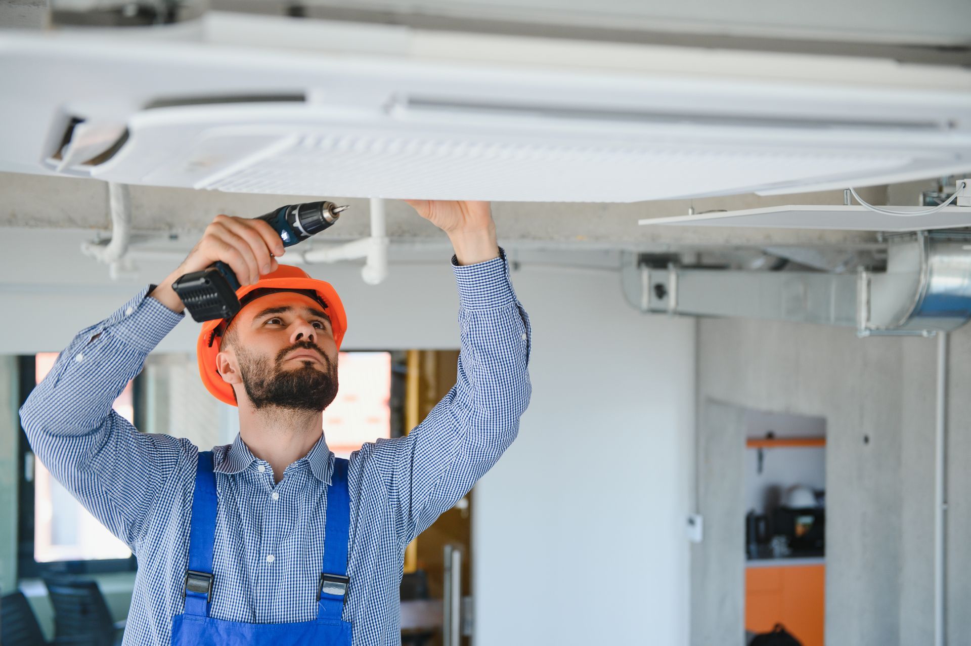 A man is working on a ceiling with a drill.