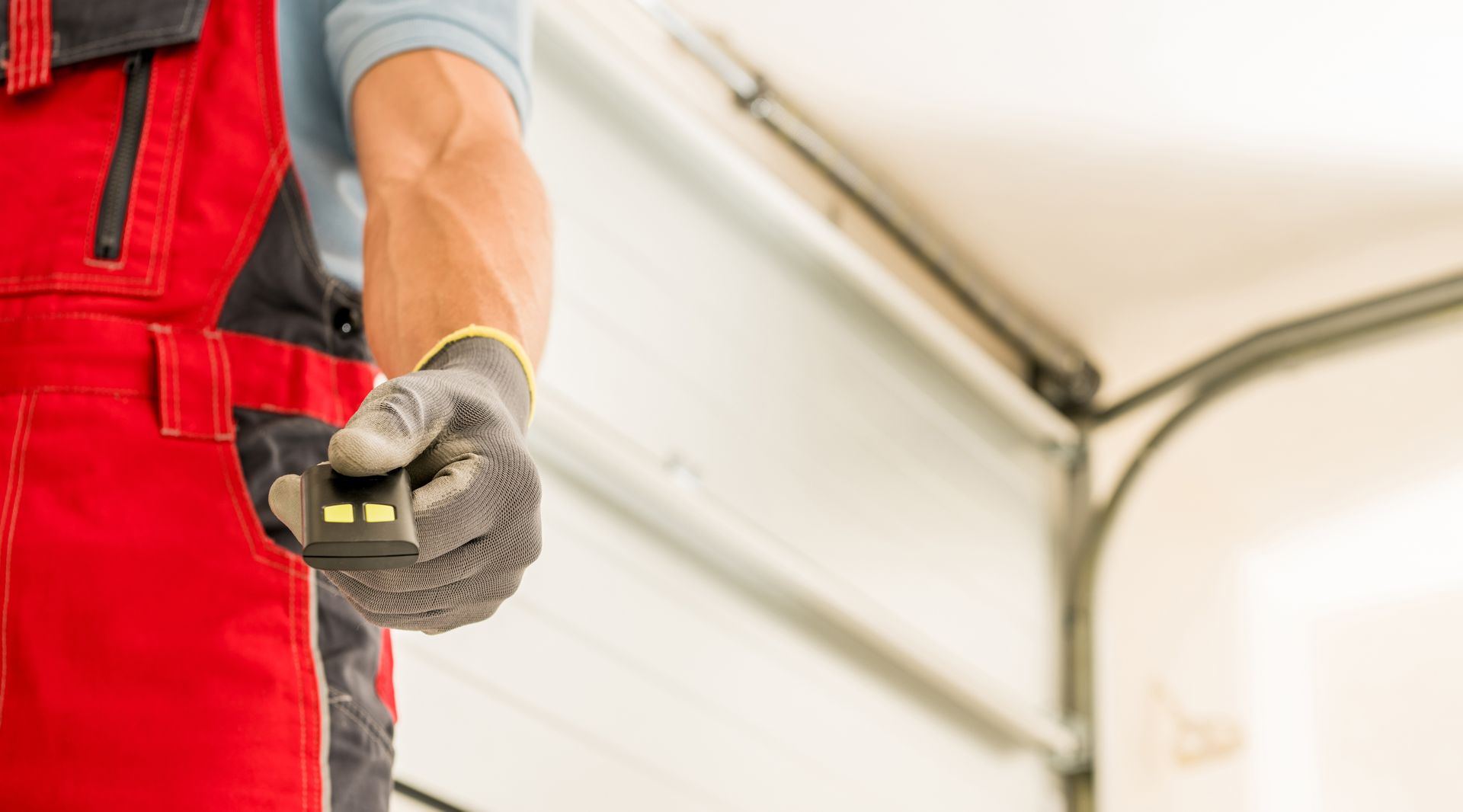 A man in red overalls is holding a remote control in front of a garage door.