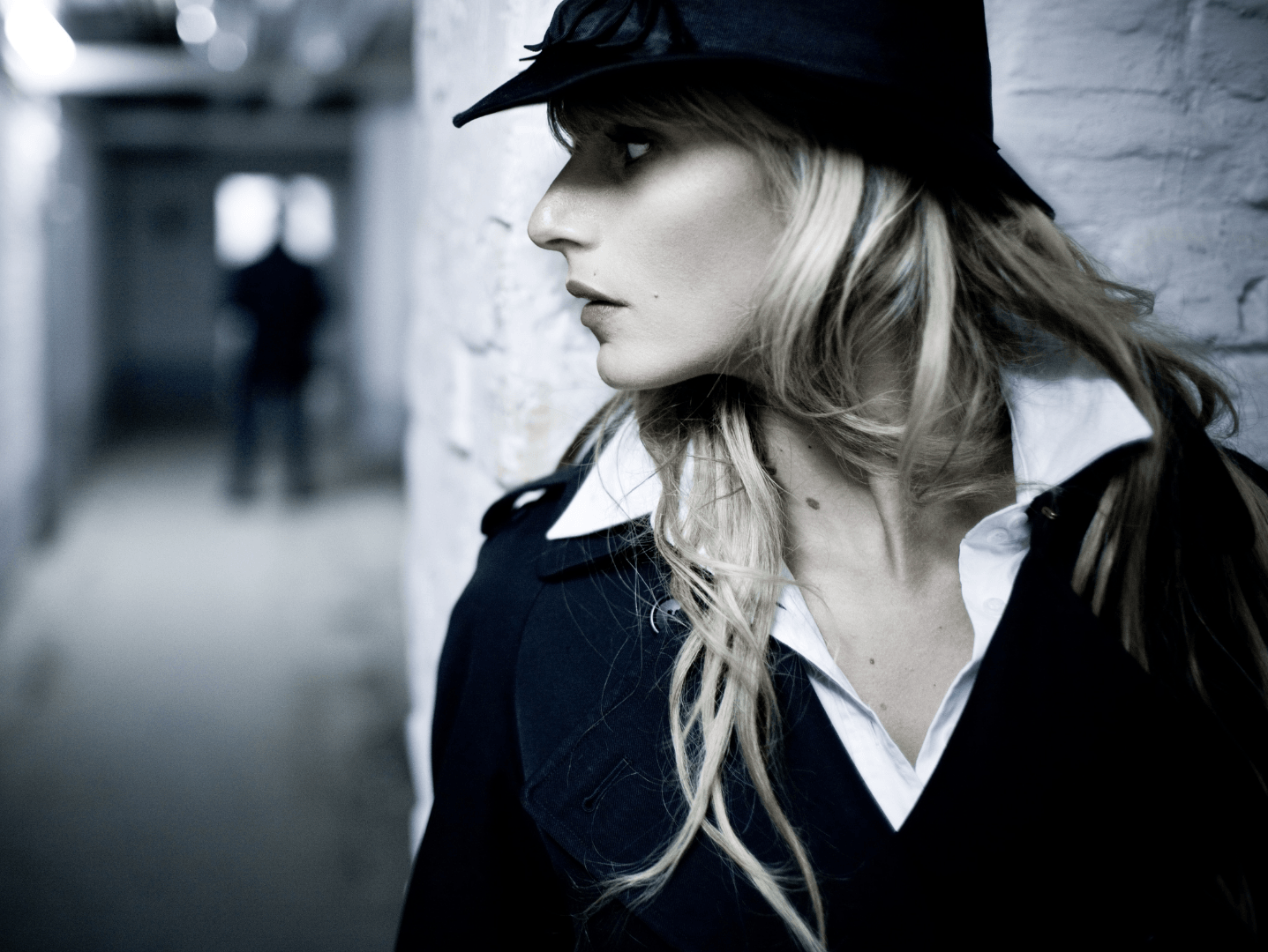 A woman wearing a hat is leaning against a wall