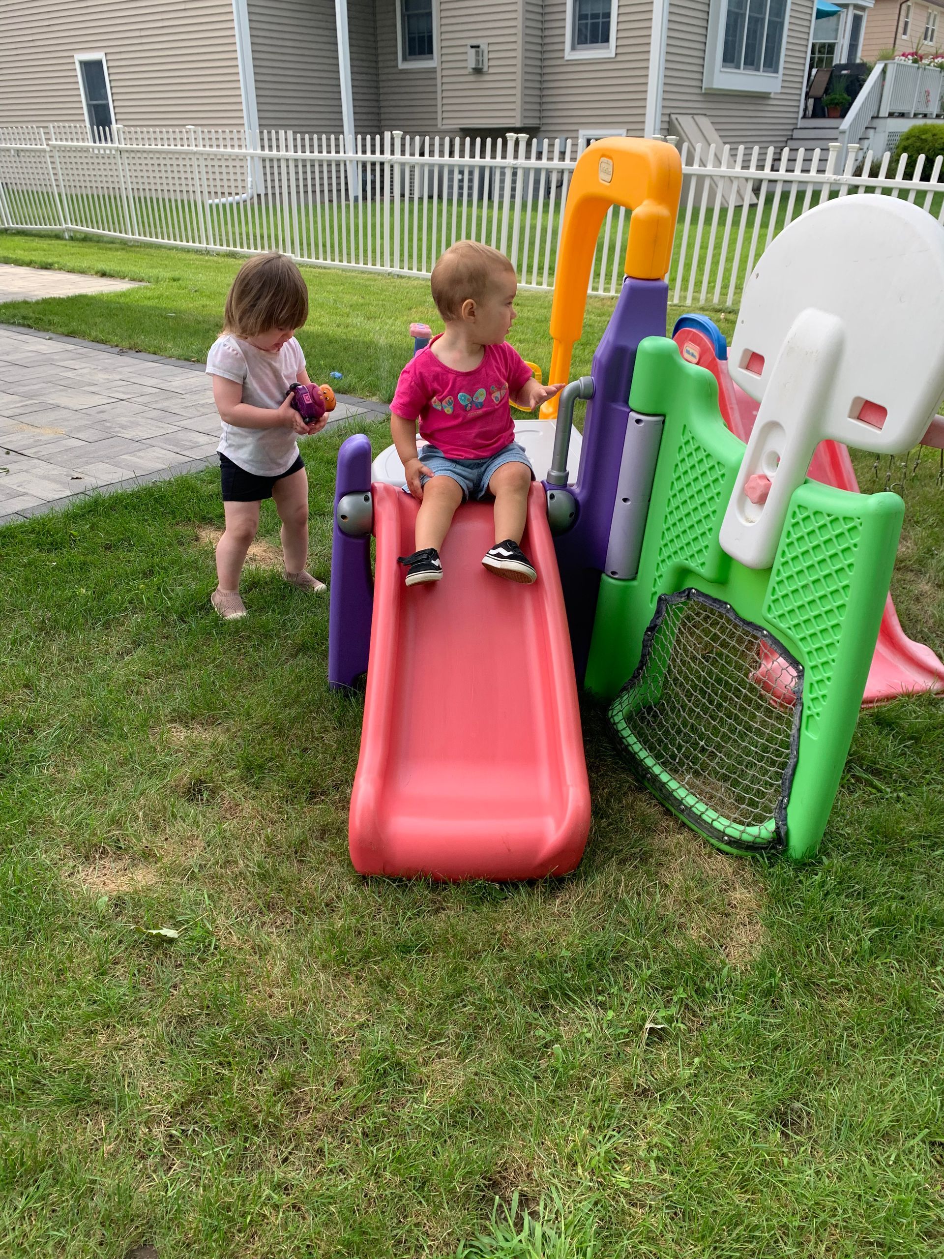 Two children are playing on a slide in a backyard.