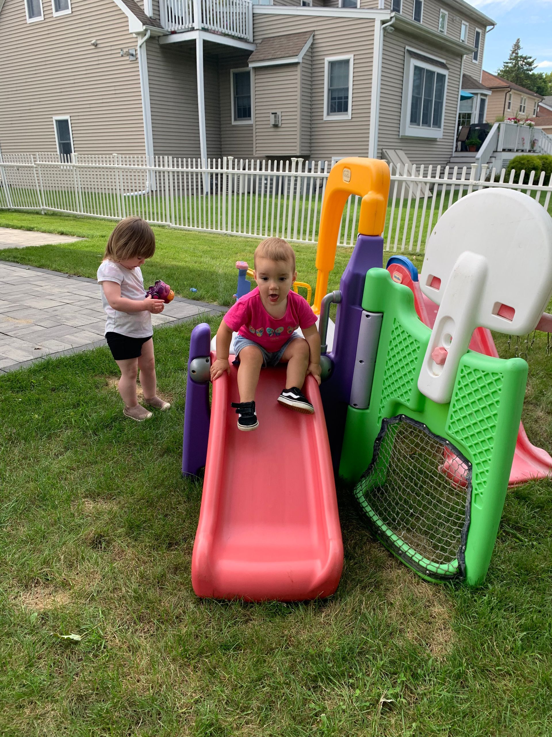 Two children are playing on a slide in a backyard.