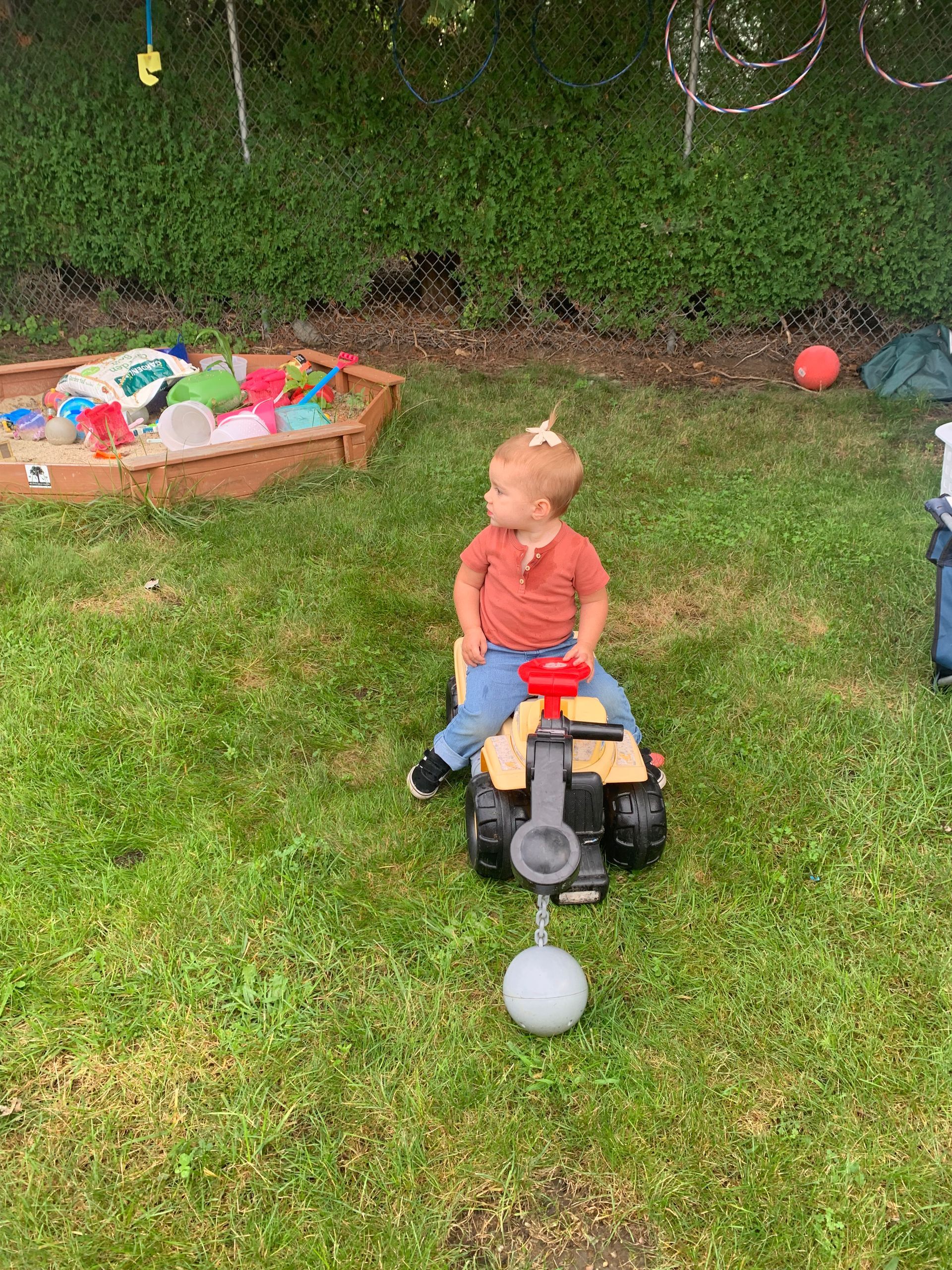 A little boy is sitting on a toy truck in the grass.