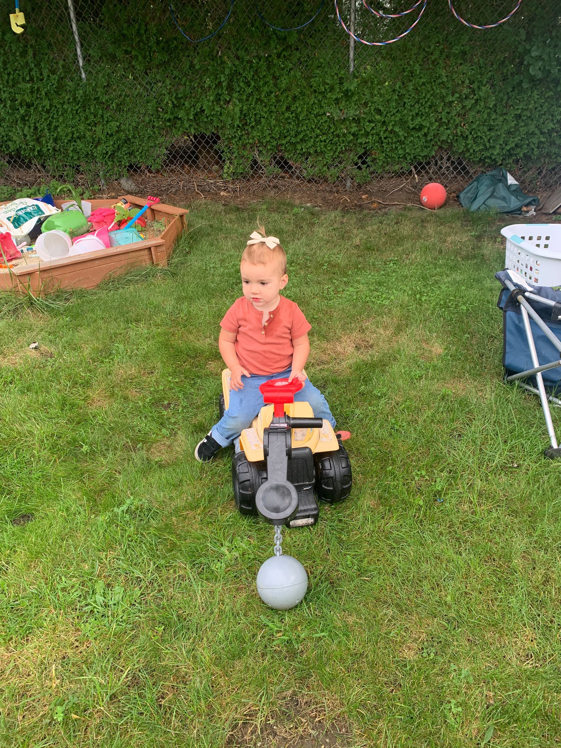 A little girl is sitting on a toy truck in the grass.