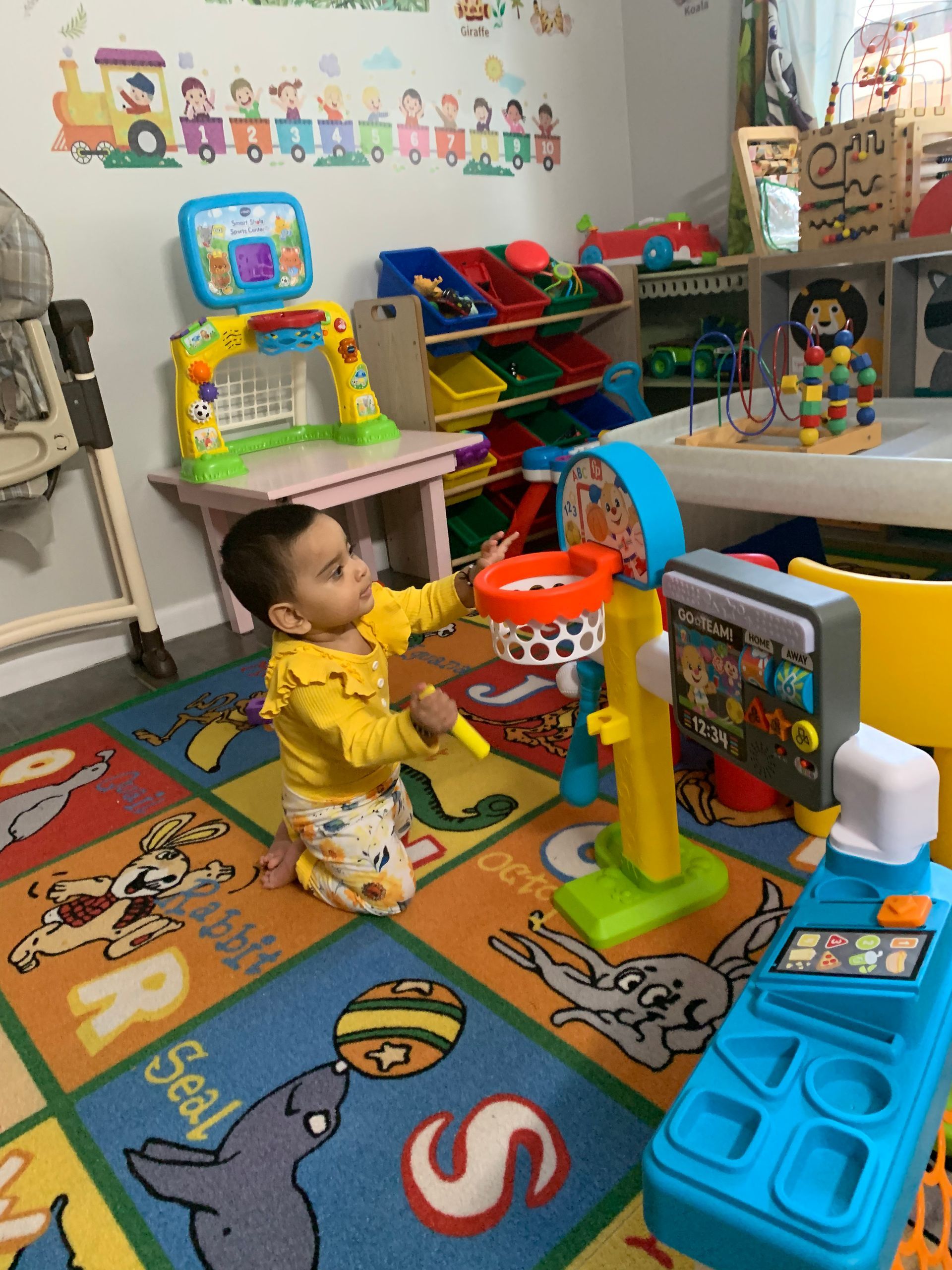 A baby is playing with a basketball hoop in a play room.