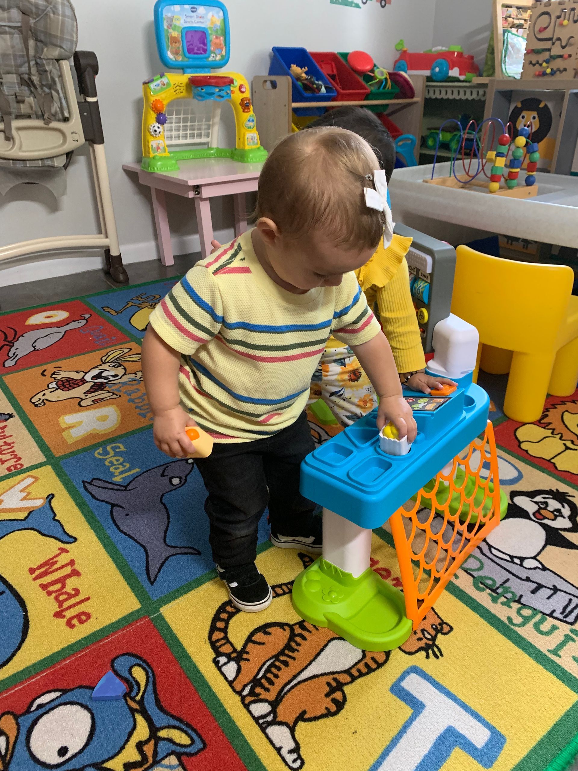 A baby is playing with a toy sink in a play room.
