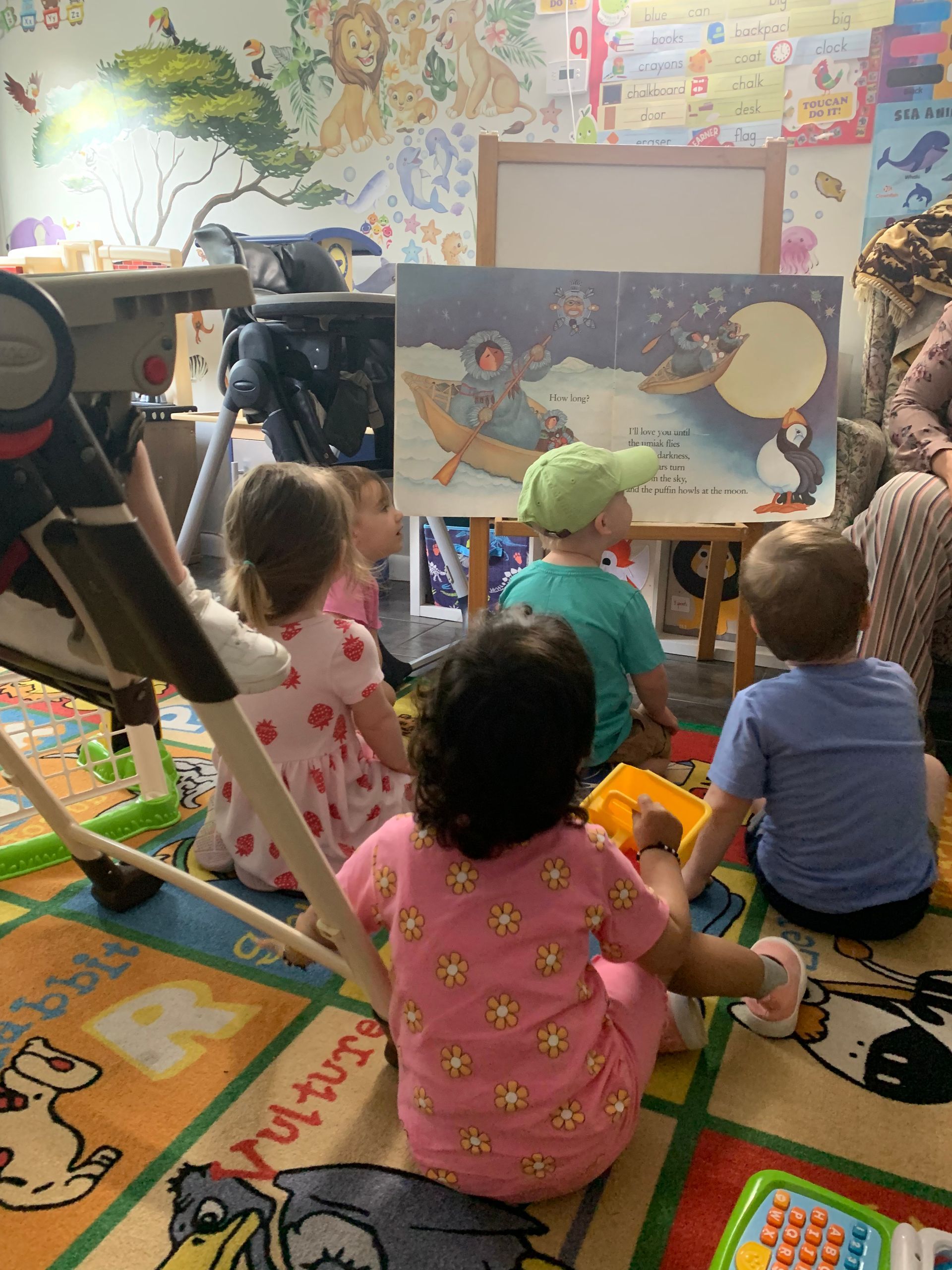 A group of children are sitting on the floor in front of a book.