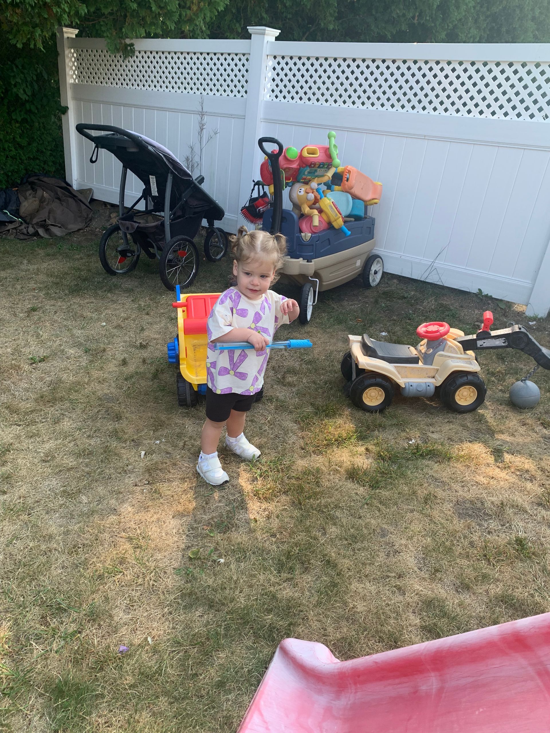 A little girl is standing in a backyard playing with toys.