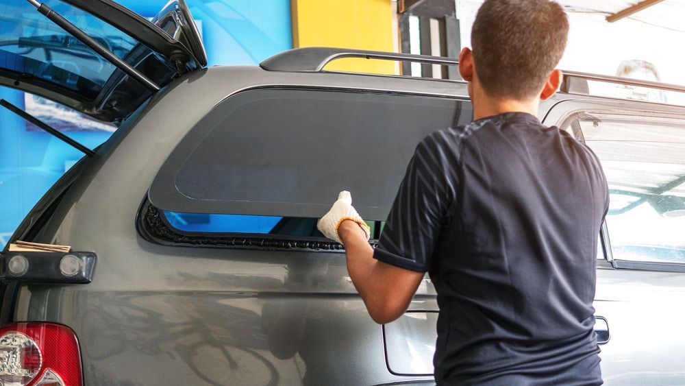 A Man is Installing a Window Tint on a Car — Bowen Mechanical & Haulage in Bowen, QLD