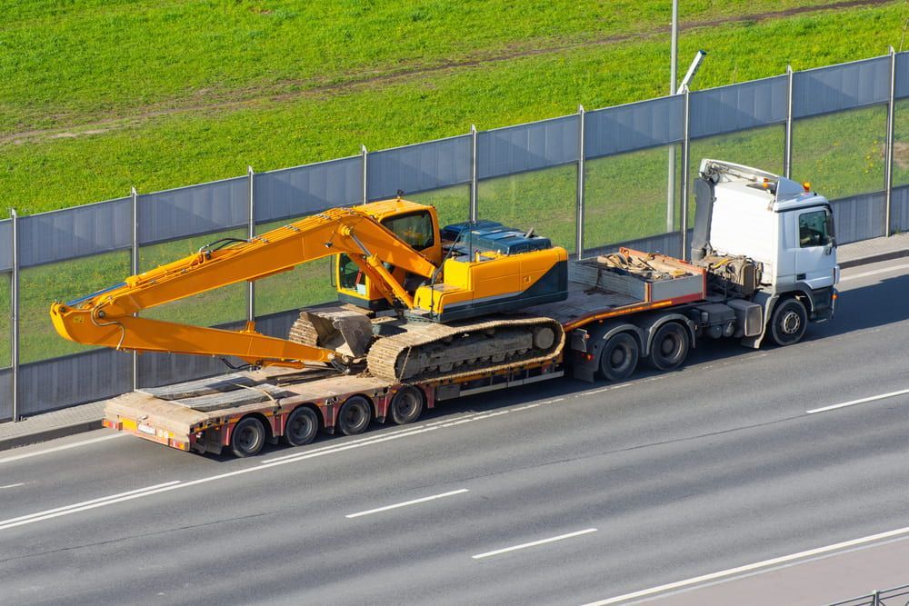 A Yellow Excavator is Being Transported on a Trailer on a Highway — Bowen Mechanical & Haulage in Bowen, QLD