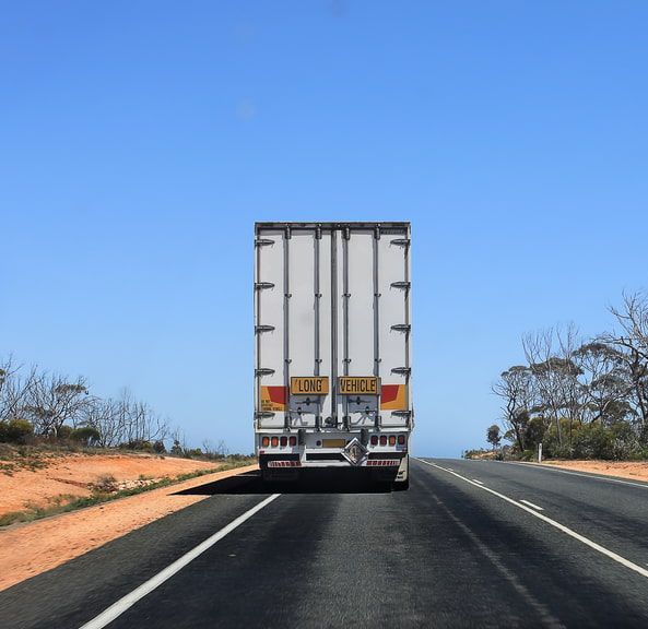 A Truck is Driving Down a Road With Trees on the Side — Bowen Mechanical & Haulage in Bowen, QLD