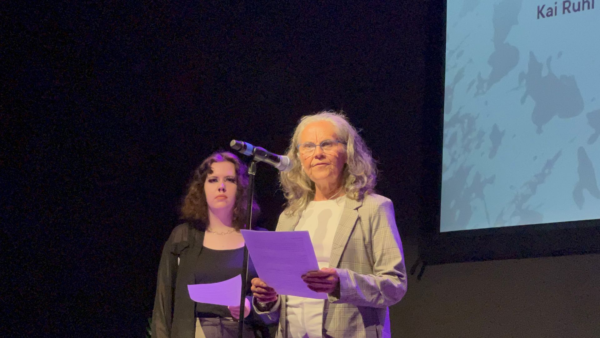 A man is sitting on a bed in a hotel room looking out the window.