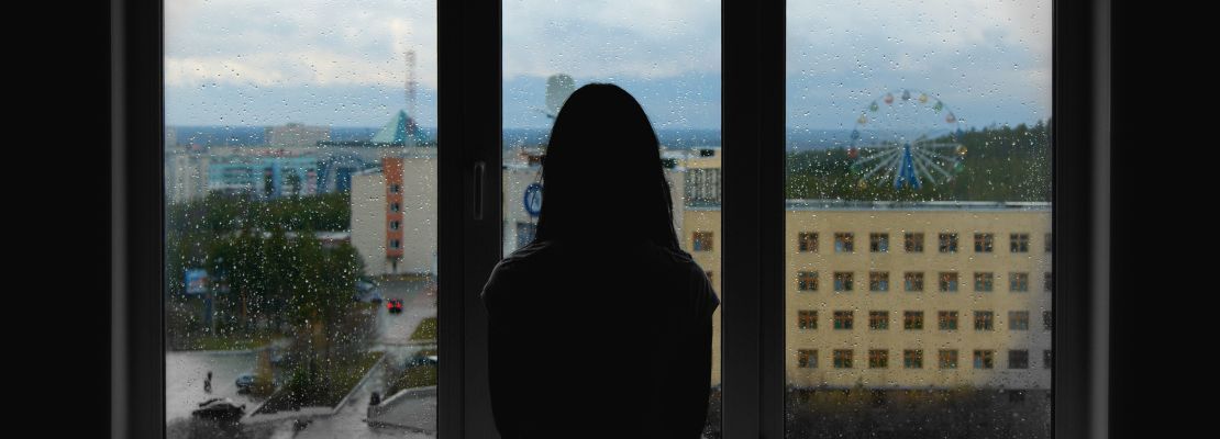 A woman is standing in front of a window looking out.