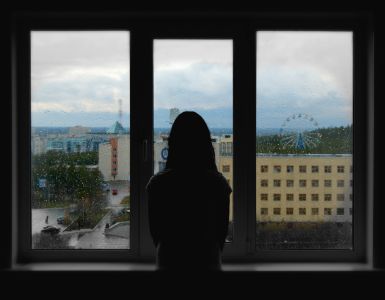 A woman is standing in front of a window looking out.