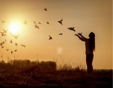 A woman is throwing birds in the air at sunset