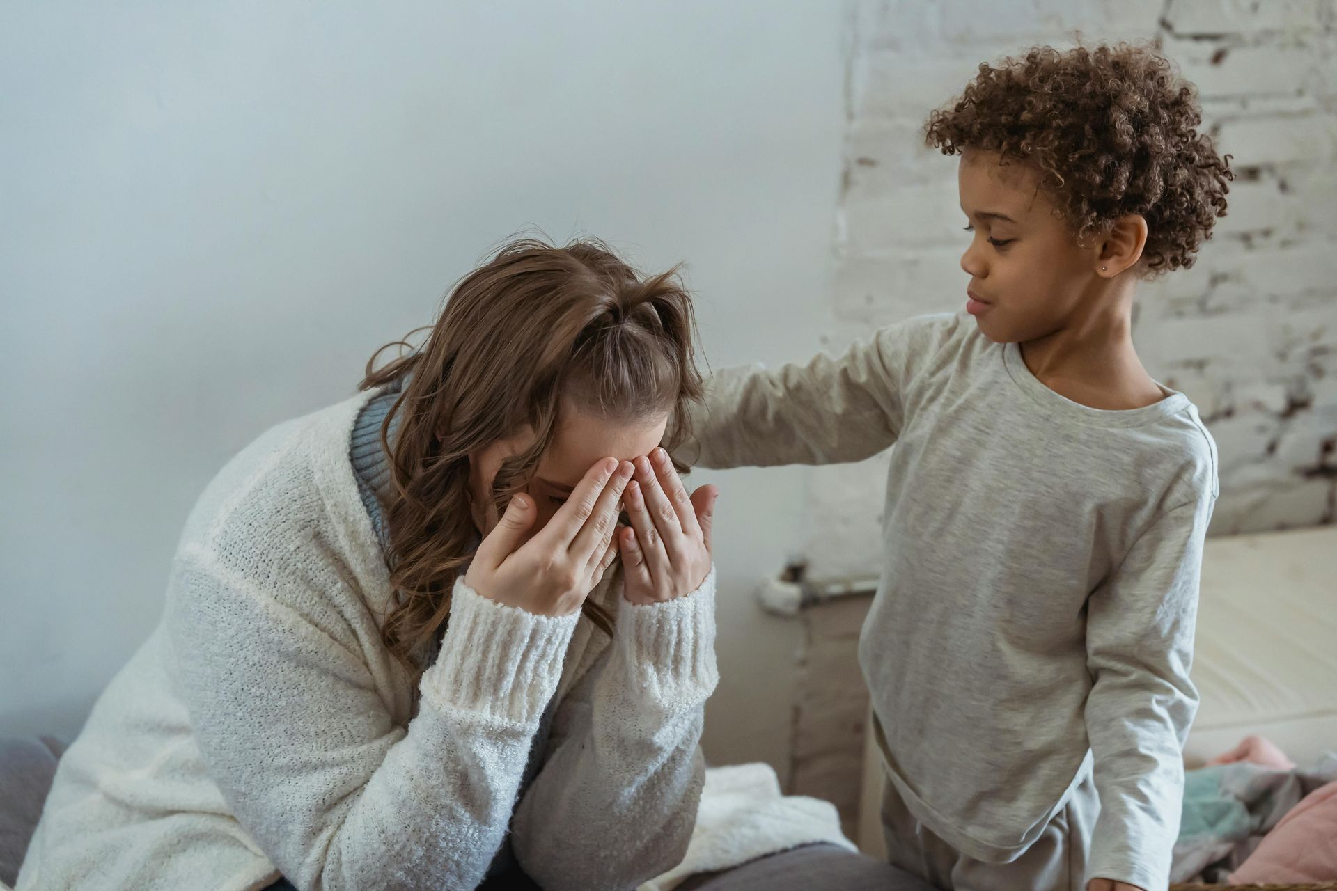 A little boy is comforting a woman who is crying on a bed.